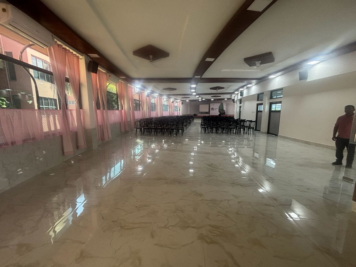 Empty indoor event space with polished floor, red curtains, tables and chairs, and fluorescent lighting