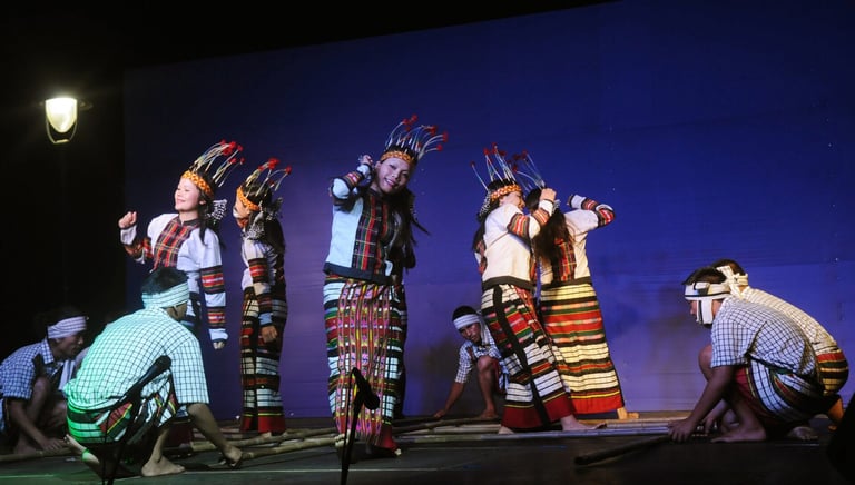 Theater performers in colorful traditional costumes on stage against a blue backdrop with dramatic lighting