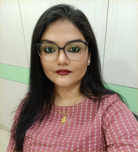 Woman with long black hair wearing glasses and a burgundy patterned top, looking at the camera in an indoor setting