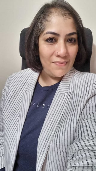 Portrait of a woman with dark shoulder-length hair wearing a gray striped blazer over a navy shirt, seated and looking at the camera