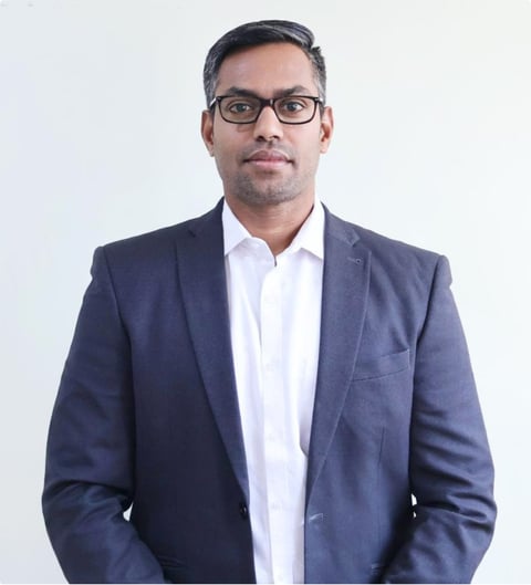 Professional headshot of a man wearing a navy blazer, white shirt, and glasses against a white background