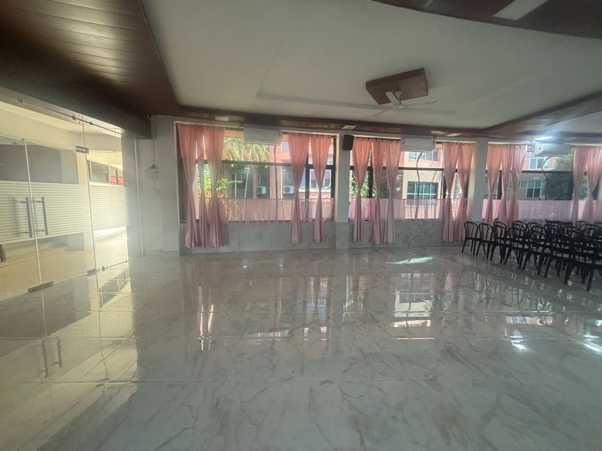 Empty event space with polished marble floor, pink curtains along windows, and rows of black chairs in the background