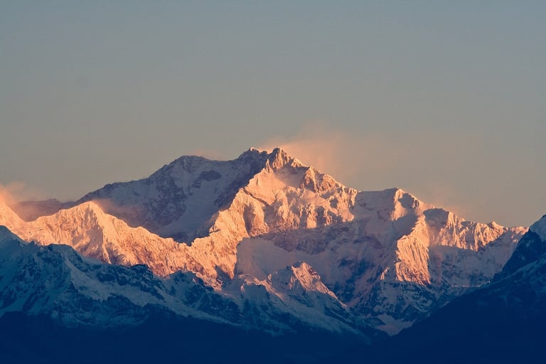 Snow-covered mountain range at sunset with warm golden light illuminating the peaks against a dusky blue sky