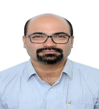 Portrait of a middle-aged man with glasses and beard wearing a light blue shirt against a white background
