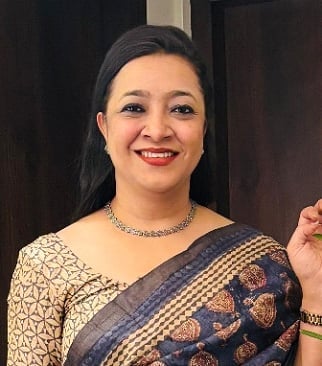 Woman wearing a blue and gold sari with red lipstick and jewelry, smiling at the camera against a dark background