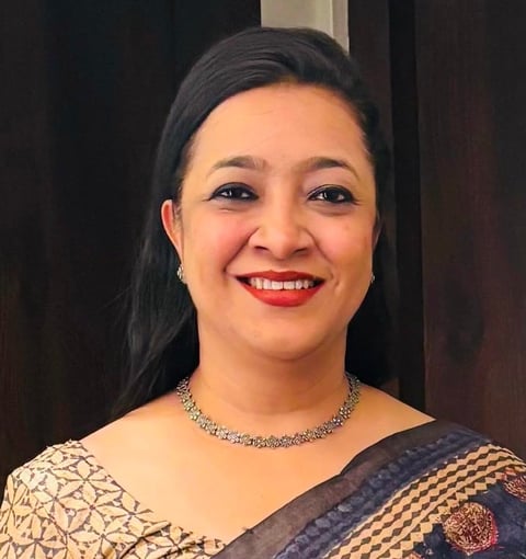 Smiling woman with dark hair wearing a diamond necklace and patterned off-shoulder blouse