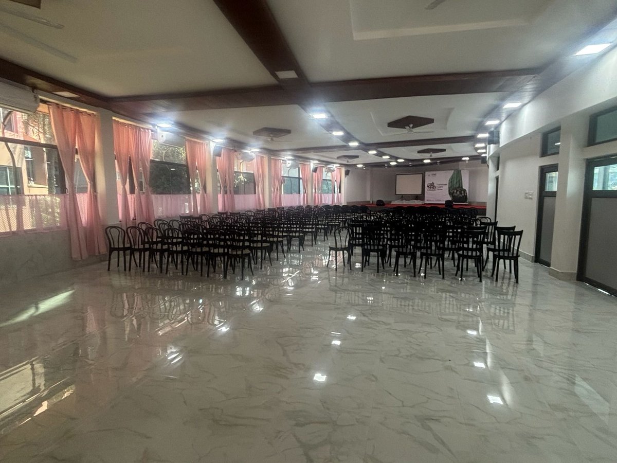 Empty event hall with polished floor, rows of black chairs, and red curtained windows