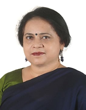 Professional portrait of a woman wearing a dark blue and green sari with drop earrings, against a white background