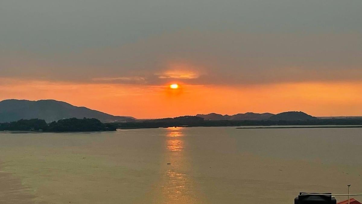 Sunset over calm water with sun reflecting on surface, silhouetted mountains in background