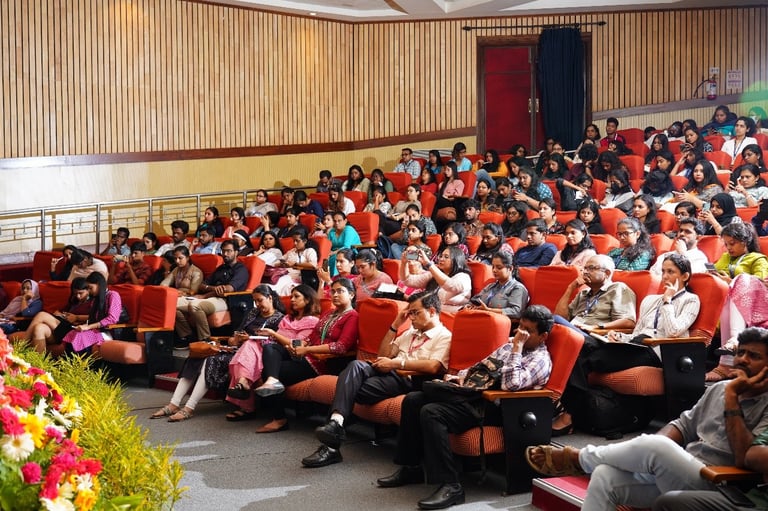 Large audience seated in red chairs in an auditorium during a presentation or event