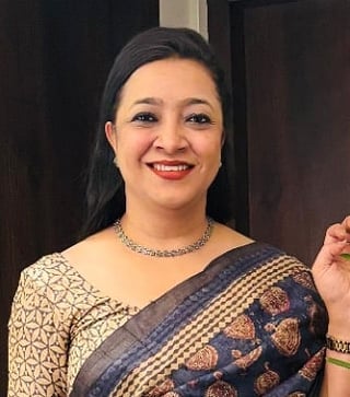 Woman wearing traditional Indian saree with gold and blue patterns, smiling at camera with red lipstick and jewelry
