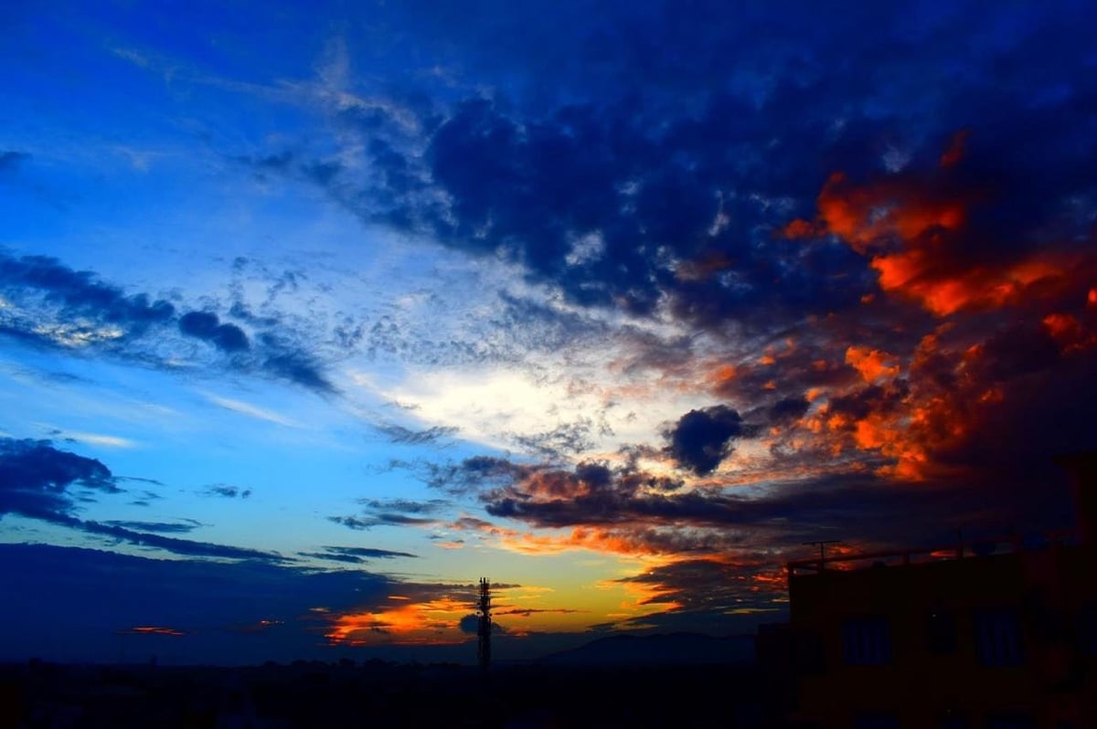 Dramatic sunset sky with vibrant orange and red clouds against deep blue twilight, silhouetted landscape below.