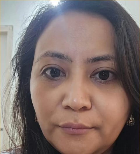 Close-up portrait of a woman with long black hair and dark eyes looking directly at the camera in an indoor setting