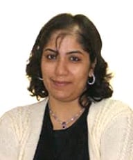 Woman with dark wavy shoulder-length hair wearing a black top and cream cardigan, smiling at camera.