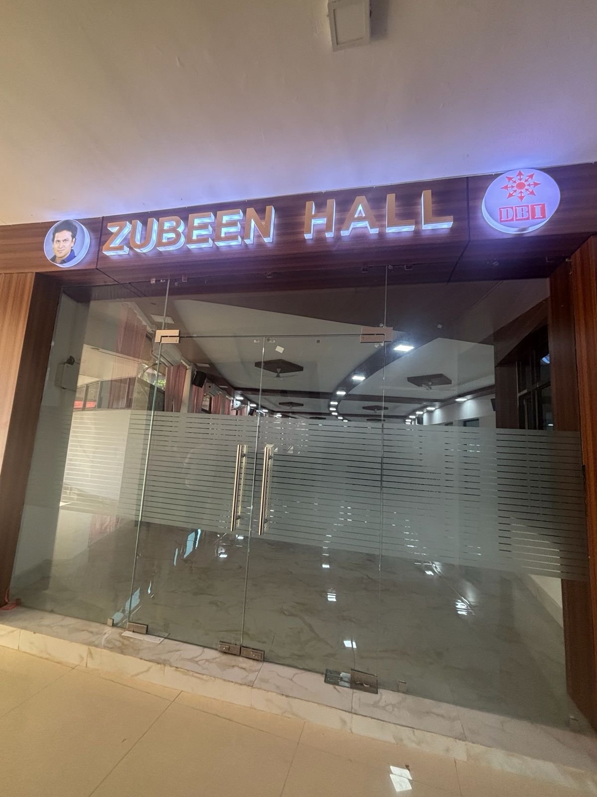 Zubeen Hall storefront with illuminated signage, glass entrance doors, and closed metal shutters