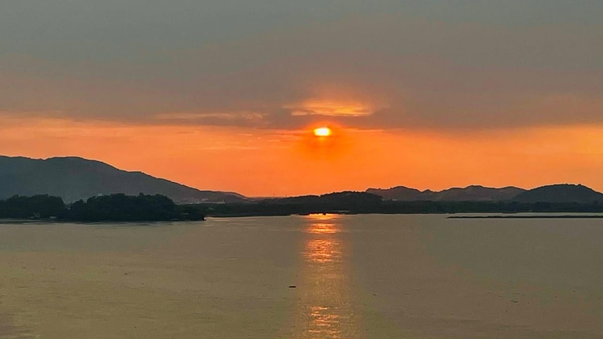 Golden sunset over a calm lake with sun reflecting on water and mountains silhouetted in the background