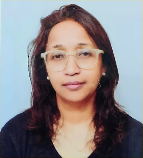 Portrait of a woman with long dark hair wearing clear-framed glasses and a black top against a light blue background