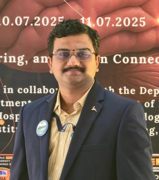 Man with mustache wearing glasses and blue blazer at conference event with dates 10.07.2025 - 11.07.2025 visible in background