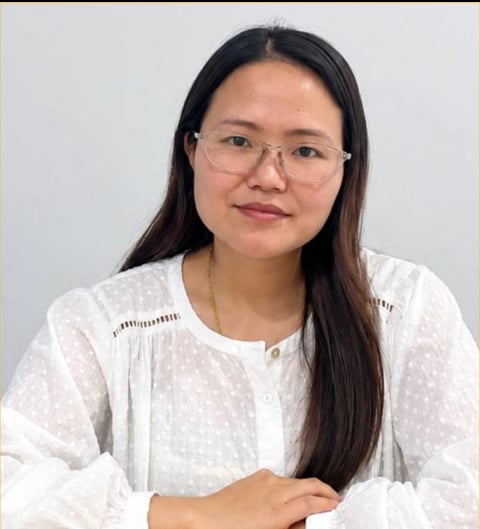 Portrait of a young woman with long black hair and glasses wearing a white textured blouse against a light background